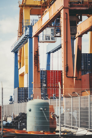 Vertical telephoto view of busy industrial shipping port with large orange and yellow gantry cranes,...
