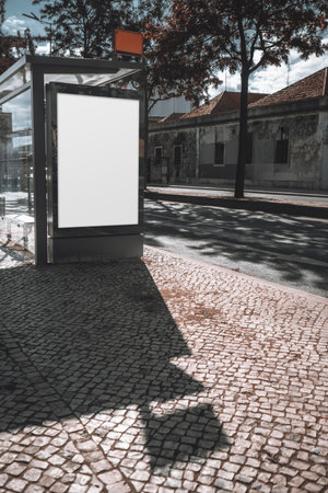Blank vertical advertising mockup on bus stop shelter, urban street, old buildings, cobblestone pavement, sunny day, shadows from trees. Ideal for advertising design presentationsの写真素材