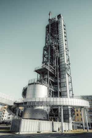 A towering industrial structure with metal scaffolding, pipes, and staircases, possibly a refinery...