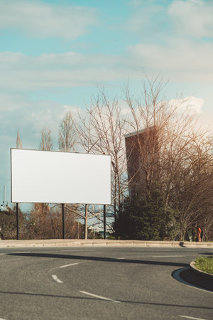 Outdoor horizontal billboard mockup on empty city street, curved asphalt road, bare winter trees, buildings in background, sunny daylight, blank space for advertising design; vertical compositionの写真素材