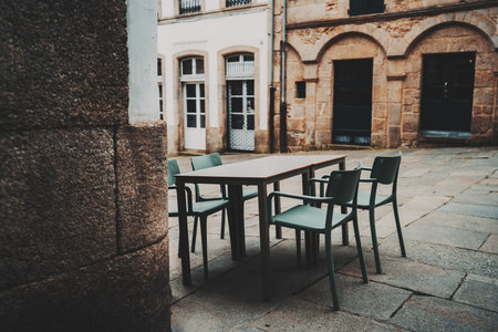 Modern outdoor dining setup in Spain with green chairs and rectangular table in cozy historic European courtyard surrounded by textured stone buildings, Santiago de Compostelaの写真素材