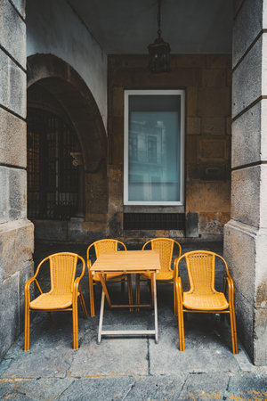 Vintage wooden table with four yellow wicker chairs on stone pavement, set under an old European...