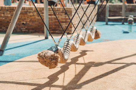 Close-up view of a row of thick rope pendulums hanging diagonally on metal cables at a modern outdoor playground with soft rubber flooring and warm natural sunlight; Punta Umbria, Spainの写真素材