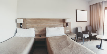 Wide-angle fisheye view of a modern hotel room with two single beds, neutral beige bedding, wooden headboard, bedside tables, two armchairs, curtain-covered window, and natural sunlightの写真素材