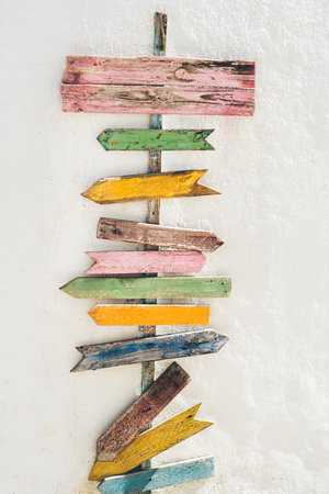 Colorful wooden directional arrows mounted on a white textured wall, ideal as a mock-up background for travel, beach, or adventure-themed text and graphic placement; vertical shotの写真素材