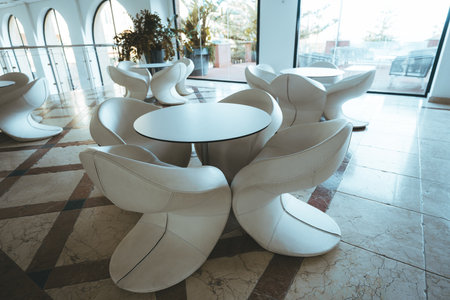 Modern lounge area with uniquely designed white sculptural chairs and round tables on a polished...