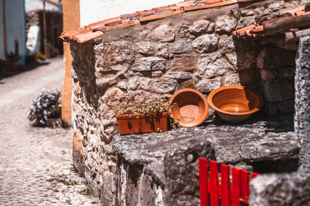 Rustic stone wall with terracotta bowls and flower pot in sunlit narrow alley of Aldeia da Mata Pequena, a traditional Portuguese village with charming historic architectureの写真素材