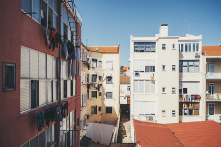 Urban residential buildings with clotheslines full of laundry drying in the sun, typical Portuguese architecture with red rooftops and blue sky, capturing daily life in a Mediterranean cityの写真素材