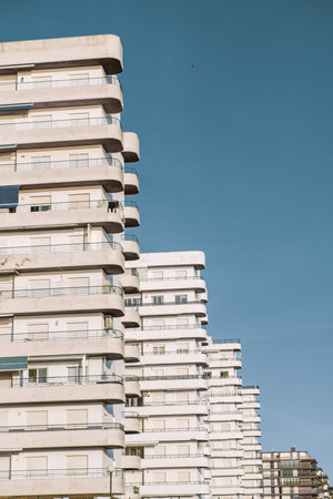 Modern white apartment buildings with rounded balconies under a clear blue sky in Punta Umbria, Spain. Bright sunlight highlights contemporary coastal architecture in vertical perspective and formatの写真素材