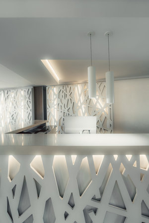 Modern hotel reception desk with abstract geometric design panels, soft ambient lighting, and minimalist pendant lights, creating a sleek and elegant welcoming interior spaceの写真素材