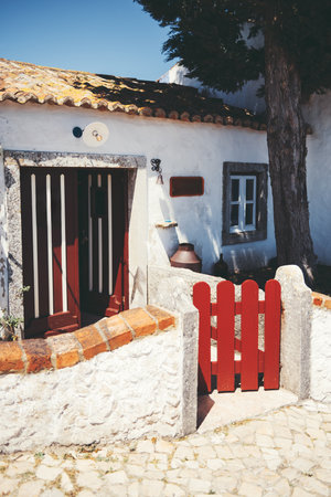 Charming traditional Portuguese countryside house in Aldeia da Mata Pequena, with whitewashed walls, red wooden gate, rustic tiled roof and cobblestone path in warm afternoon sunlightの写真素材