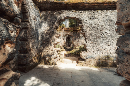 Sunlit interior of an ancient stone ruin with arched Gothic windows, textured crumbling walls, and overgrown greenery, creating a mystical and historical atmosphere in Sintra, Portugalの写真素材