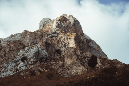 Rugged limestone peak in Picos de Europa National Park, northern Spain, with dramatic textures, rocky cliffs, and patches of vegetation under a cloudy sky, evoking natural majesty and adventureの写真素材