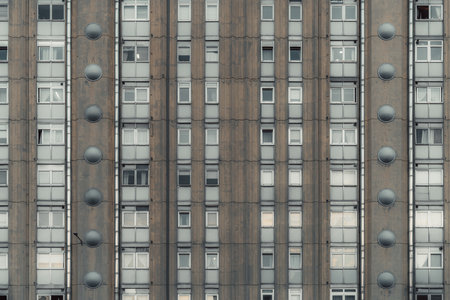 Facade of an old brutalist-style apartment building with repetitive geometric windows and circular ventilation elements, showcasing urban decay, symmetry, and architectural minimalismの写真素材