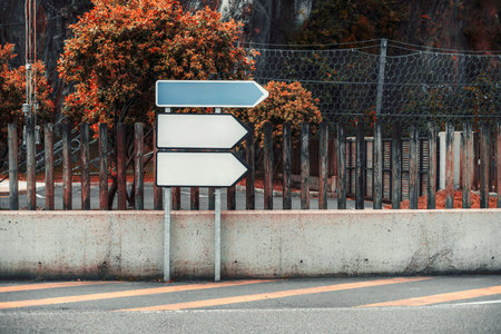 Set of three blank empty directional arrow road signs mounted on metal poles, ideal for mockups or design templates, placed against rustic wooden fence and autumn foliage backgroundの写真素材