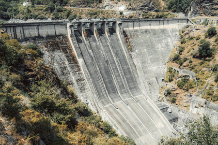 Massive concrete dam structure integrated into a rugged mountainous landscape, featuring multiple...
