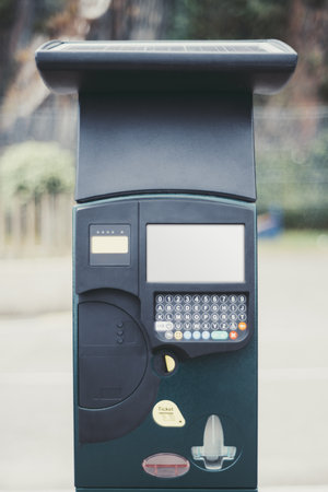 Modern solar-powered parking meter with keypad, digital display, and ticket dispenser, standing on a street with defocused urban background, offering contactless payment solutionの写真素材