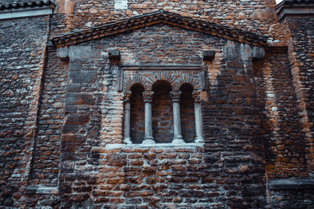 Detailed view of a historic Romanesque stone wall with triple-arched window and decorative columns in Asturias, Spain, showcasing medieval architecture and textured masonry in moody lightの写真素材