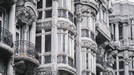 Ornate classical facade of a historic European building with carved stone reliefs, curved wrought-iron balconies, and aged white window frames, evoking timeless elegance and architectural grandeurの写真素材