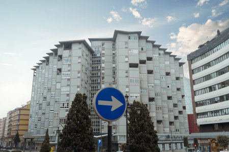 Symmetrical brutalist apartment block dominates Oviedo skyline, its pale concrete grid offset by a blurred blue right-arrow traffic sign in the foreground and soft morning sky copy space aboveの写真素材