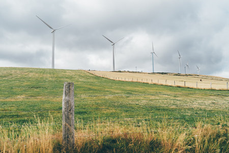 Wind turbines standing tall on rolling autumn fields, generating renewable energy under dramatic...