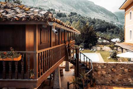 Traditional wooden horreo in Asturias converted into cozy living space, surrounded by rustic stone walls, garden, and pool, with scenic mountain landscape in the background; wide-angle shotの写真素材