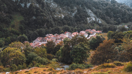 Scenic aerial view of the picturesque autumn village of Tielve in Asturias, Spain, nestled deep in lush green mountains and dense forest, showcasing red-tiled rooftops and peaceful rural charmの写真素材