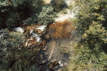 Crystal-clear mountain stream flowing through rocky terrain and dense green foliage, with sunlight highlighting the textures of submerged stones and gentle ripples in northern Spain's wildernessの写真素材