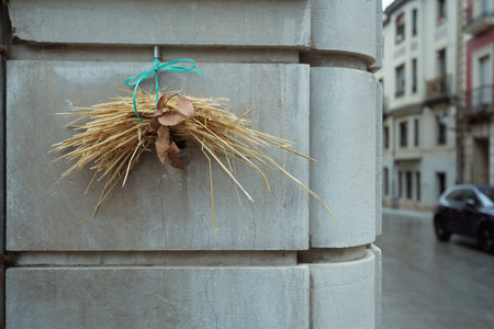 Rustic straw bundle with dried leaves tied by green twine hangs on a stone wall corner in Asturias, Spain; urban street background, minimal composition with texture and copy spaceの写真素材
