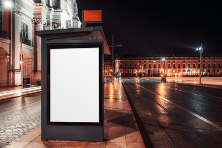 Blank illuminated billboard mockup on a city street bus stop at night with reflections on wet pavement, historic architecture, and blurred lights of passing traffic in urban background; long exposureの写真素材