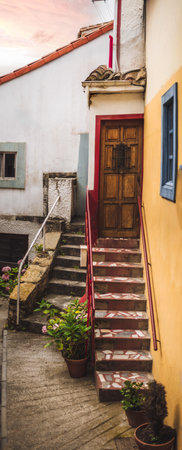 Vertical panorama of a rustic narrow alley in Cudillero with stone steps, wooden door, potted plants, and colorful facades, captured with shallow depth of field for artistic focusの写真素材