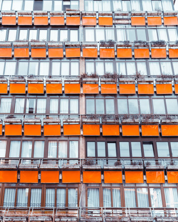 Modern apartment building facade with repeating orange balcony panels and glass windows, creating a...