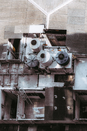 Top view of urban rooftop with metal water tanks, pipes, ladders and weathered corrugated roofs, showing industrial textures and geometry in warm afternoon lightの写真素材