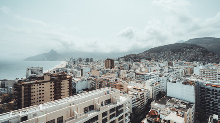 Wide-angle aerial view of Rio de Janeiro coastline with Ipanema Beach, city buildings, and lush mountains under cloudy sky, capturing the vibrant urban and natural landscape of the Brazilian coastの写真素材