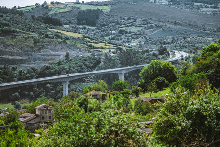 Long concrete viaduct stretching across lush green mountain valley, seen through telephoto lens with...