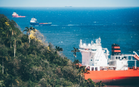 Large red oil tanker anchored near lush tropical coastline in Brazil, surrounded by deep blue ocean and distant cargo ships under bright sunlight, concept of global trade and maritime transportの写真素材