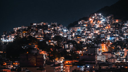 Night view of Pavao Pavaozinho favela in Rio de Janeiro, Brazil, captured with long exposure, glowing city lights illuminating hillside houses against dark mountain silhouetteの写真素材