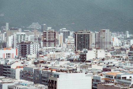 Daytime cityscape of Rio de Janeiro with dense modern buildings, high-rises and residential blocks against a hazy green mountain backdrop, capturing the urban rhythm of Brazilの写真素材