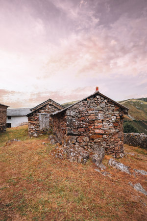 Rustic stone houses in the Asturian mountains of Spain, illuminated by warm sunset light under a colorful sky, representing traditional rural architecture on the Camino de Santiago; wide-angle viewの写真素材