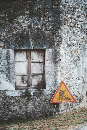 Weathered construction sign leaning against an old stone wall with a sealed wooden window. Rustic texture, muted tones, and natural decay create a nostalgic countryside atmosphereの写真素材