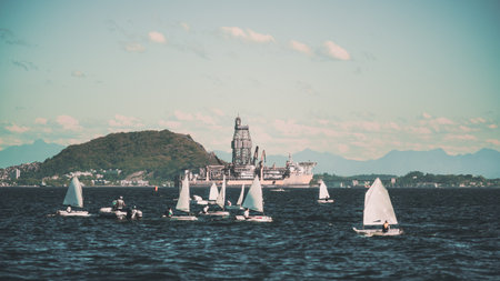 Small sailboats in a defocused foreground gliding across dark rippling water, with selective focus a...