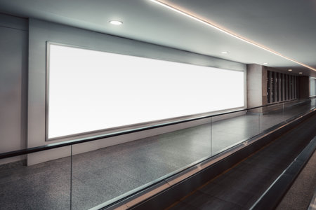 Large bright mock-up billboard beside an airport-style travelator in a clean modern corridor, illuminated by soft ceiling lights and offering spacious template space for advert design; banner templateの写真素材