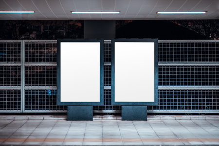 Urban mock-up scene with two blank vertical billboard posters templates at an outdoor subway platform, illuminated frames against metal grid wall, tiled floor and fluorescent lightsの写真素材