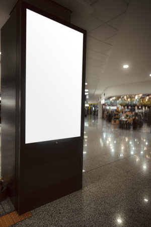 Blank vertical advertising lightbox mock-up in modern shopping mall interior, empty white screen with copy space, glossy floor reflections, indoor promotional display for branding and marketingの写真素材