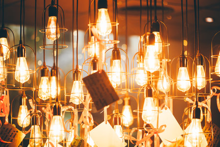 Festive New Year decor with glowing Edison bulb in metal cage, hanging pendant light on cord with ribbon and wish tag, warm golden bokeh illumination for party interiorの写真素材