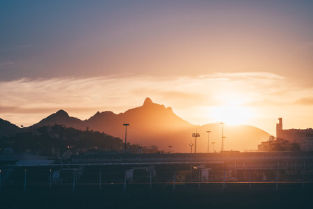 Telephoto view of sunrise over Rio de Janeiro mountains behind an airport runway and fence, warm...