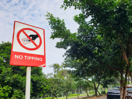 No Tipping sign at the parking area of public place, with blue sky and green tree tops as background.の写真素材