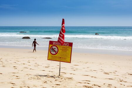 Warning sign on the beach swimming prohibited is disregarded by a man