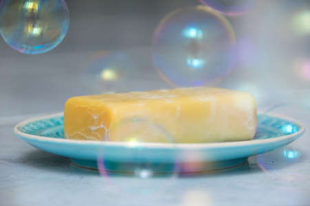 Yellow soap on a turquoise plate, around it soap bubbles float to the groundの写真素材