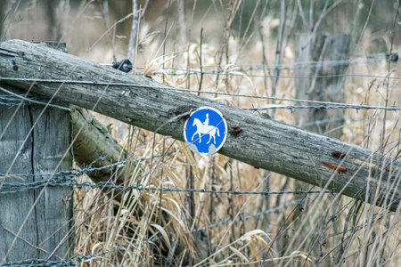 A blue equestrian sign on a wooden fence by the dirt roadの写真素材